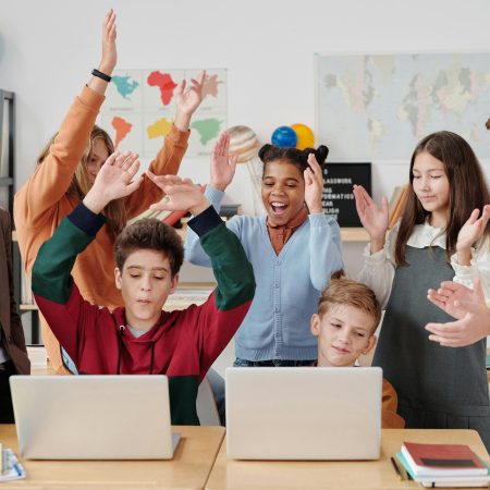 A group of happy students and a teacher clapping together in a school classroom.